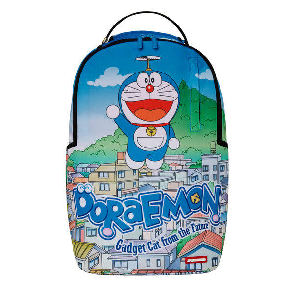 Sprayground DLSXR backpack featuring Doraemon flying over a colorful cityscape with blue sky and the words “Doraemon: Gadget Cat from the Future” across the front.