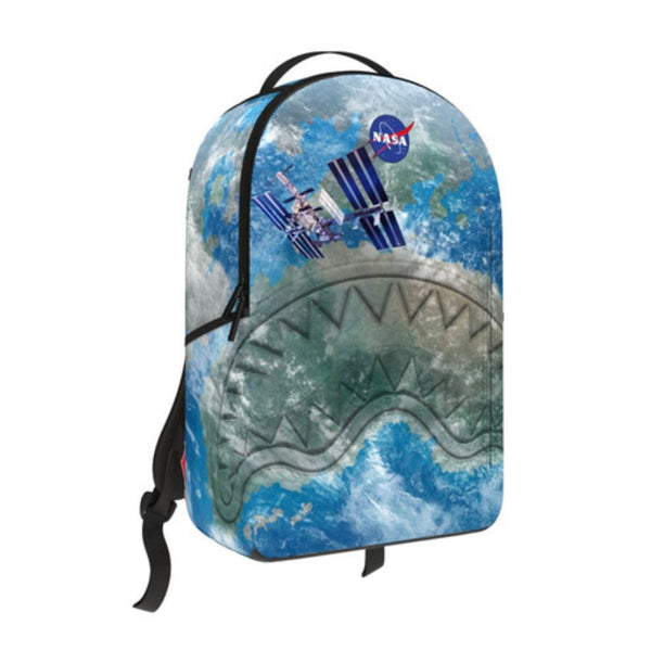 Sprayground DLXSR Backpack featuring the NASA International Space Station graphic with black and metallic detailing, official NASA patch, gold zippers, and multiple compartments.