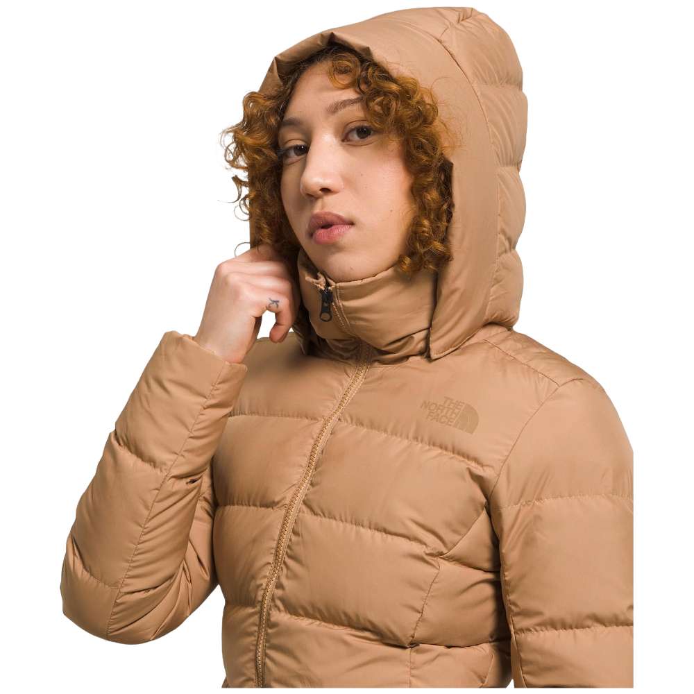 A stylish North Face Women's Metropolis Jacket in almond butter worn by a woman against a snowy backdrop.