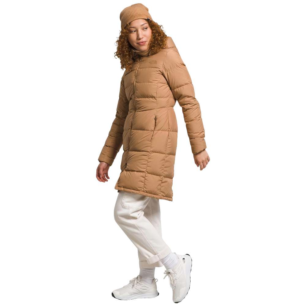 A stylish North Face Women's Metropolis Jacket in almond butter worn by a woman against a snowy backdrop.