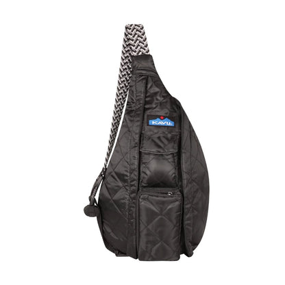 Compact black quilted KAVU sling bag with rope-style shoulder strap worn crossbody on a person, showing multiple zip compartments and casual outdoor styling.
