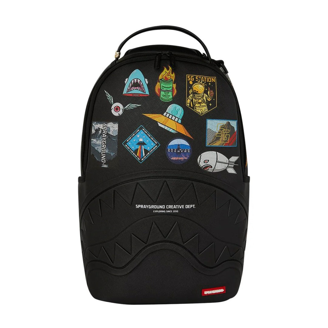 SPRAYGROUND Sharkmouth Embossed W/ Patches DLXSV Backpack featuring embossed shark-mouth design with colorful patches on black vegan leather and SPRAYGROUND logo detailing.